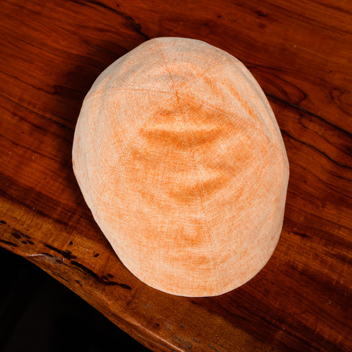 A light orange-colored textured fabric skullcap or prayer cap resting on a dark brown wooden surface.