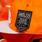 Close-up of an orange snapback cap with a white flat brim and a black sewn-on brand tag reading Hales.