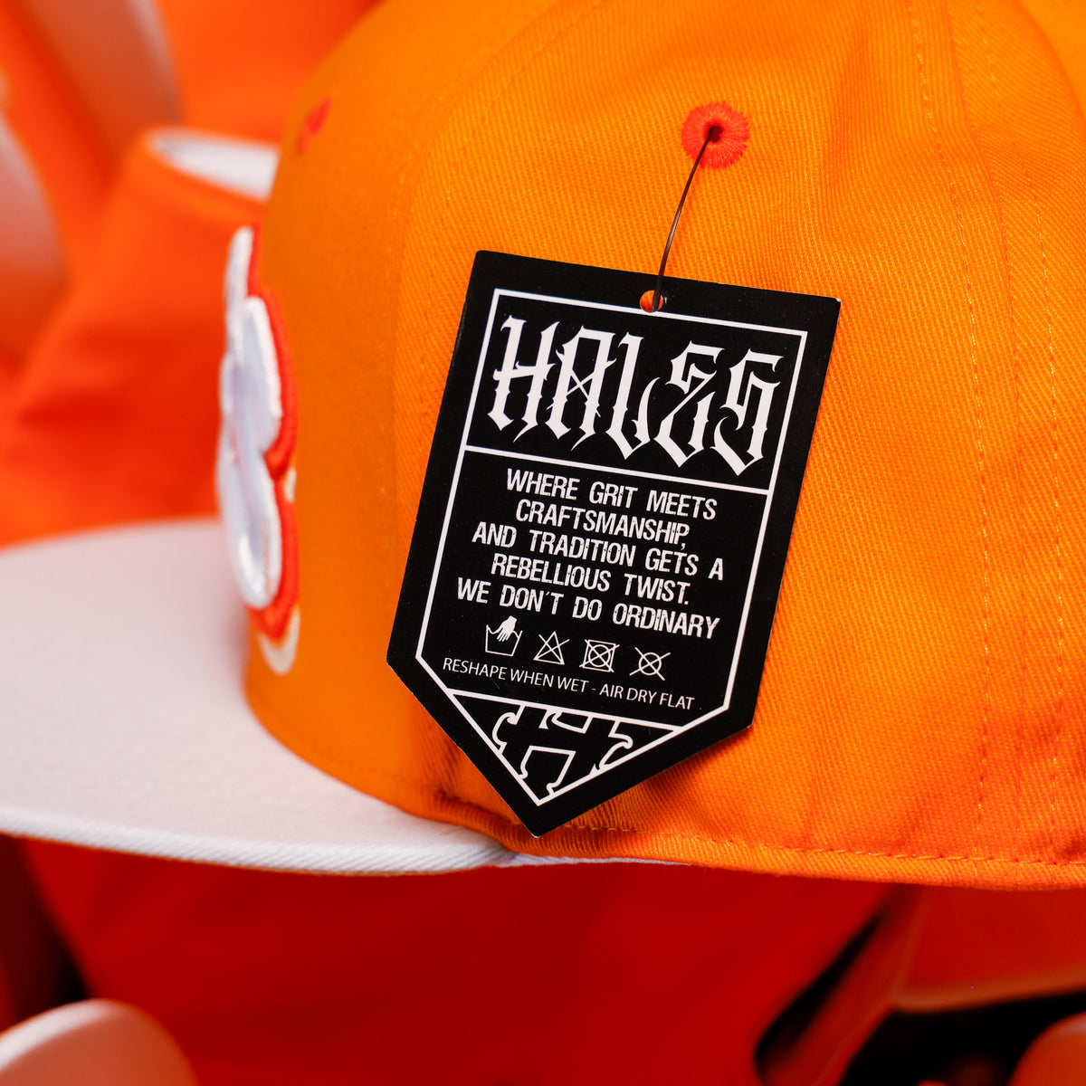 Close-up of an orange snapback cap with a white flat brim and a black sewn-on brand tag reading Hales.