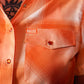 Close-up of an orange and peach plaid short-sleeve button-up shirt by Hales, featuring a chest pocket with a snap closure and a visible Hales brand tab.