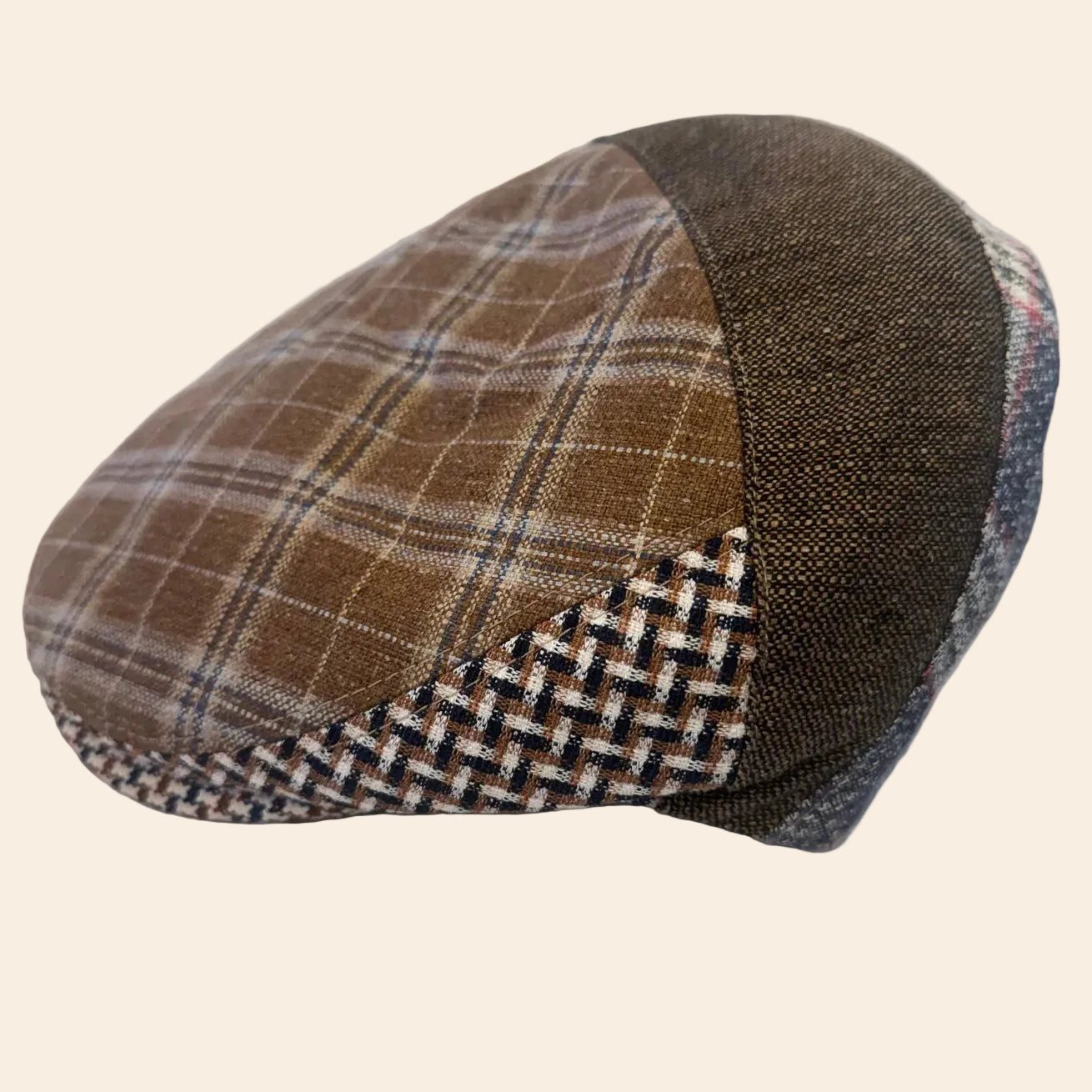 A brown and beige plaid flat cap with a textured dark brown side panel and a woven patterned band, resting on crumpled white tissue paper.