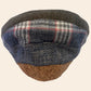 A low-profile flat cap hat featuring a textured dark gray and navy woven fabric top, a plaid pattern band in gray, white, and red, and a natural cork base.