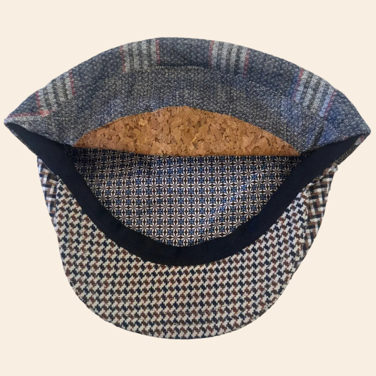 A vintage-style flat cap with a blue and beige houndstooth patterned brim, a patterned blue and gray crown, a black fabric trim, and a natural cork lining.