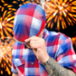 Person wearing a red, white, and blue checkered hat and shirt with fireworks in the background