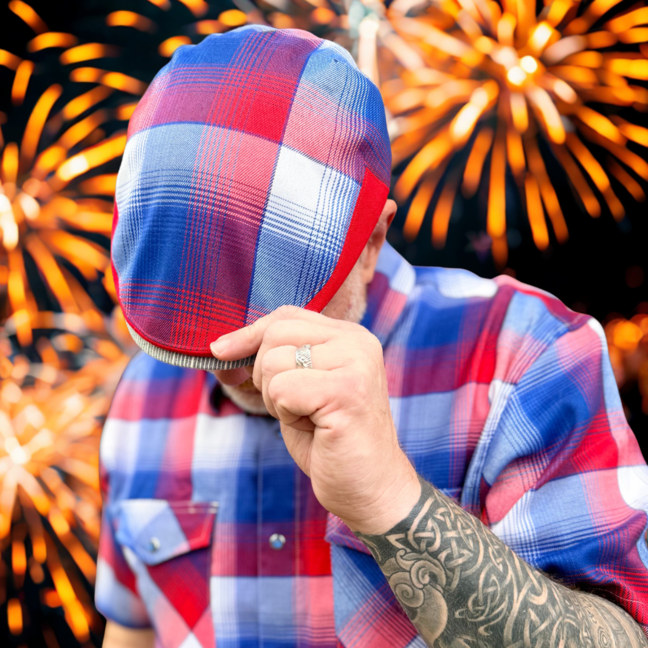 Person wearing a red, white, and blue checkered hat and shirt with fireworks in the background