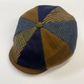 A vintage-style flat cap made of patchwork fabrics, featuring brown suede-like panels, navy blue solid panels, and tweed plaid panels in green and brown, with a matching button on top, set against a plain white background.