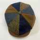 A handmade flat cap made of multiple fabric panels, featuring navy blue solid, brown wool, and green-and-brown houndstooth tweed sections, with a matching brown visor and button.
