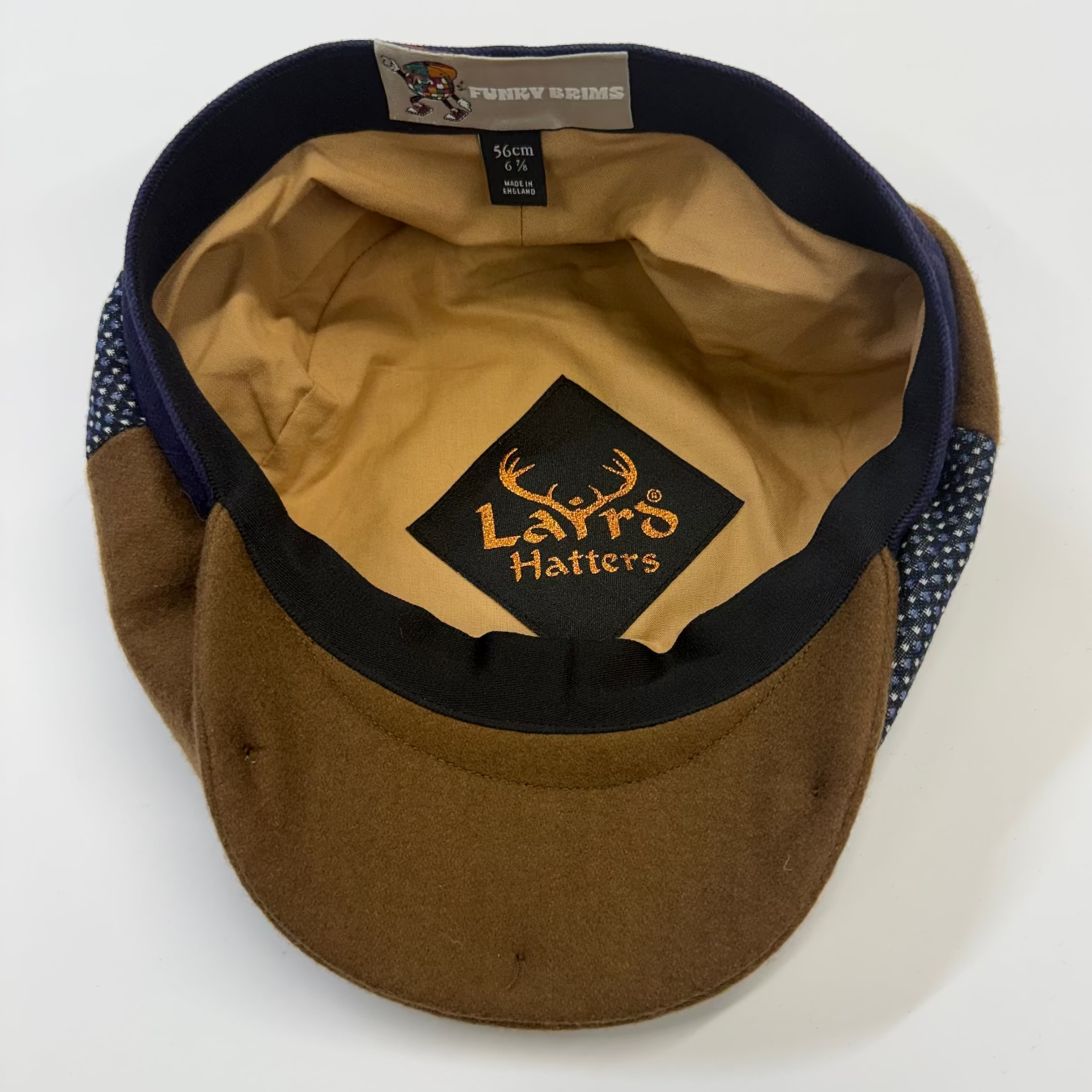 A brown wool cap with a tan interior, navy blue trim, and a patterned fabric side panel. The interior features a black patch with the brand name 'Laird Hatter's' in gold.