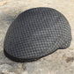 A dark gray and black houndstooth pattern flat cap resting on a textured stone surface.