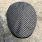 A gray and black textured flat cap resting on a natural stone surface.