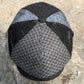 A structured flat cap hat with a black and gray houndstooth pattern on the front and brim, and light gray patterned side panels, resting on a textured stone surface.