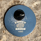 A round blue model kit pinback badge with a black center hole, featuring the text 'FUNNYBRIMS 1/200' and a globe graphic, photographed on a textured stone surface.