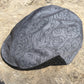 A gray cycling cap with a black and gray swirling pattern, resting on a textured concrete surface.