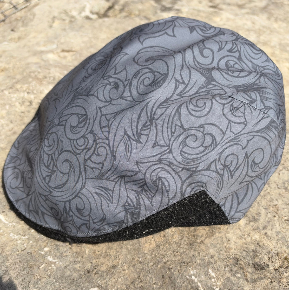 A gray cycling cap with a black and gray swirling pattern, resting on a textured concrete surface.