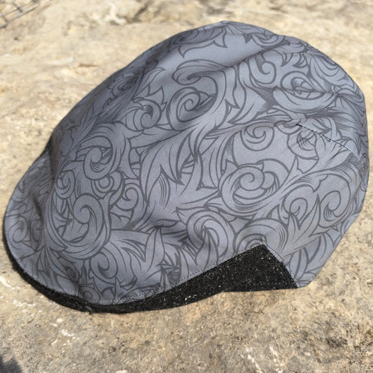 A gray cycling cap with a black and gray swirling pattern, resting on a textured concrete surface.
