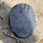 A gray protective helmet cover with a black floral scroll pattern, resting on a textured gray stone surface.