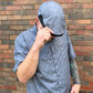 A man wearing a light blue patterned button-down shirt and a matching light blue hooded cap with a black trim, posing in front of a brick wall.