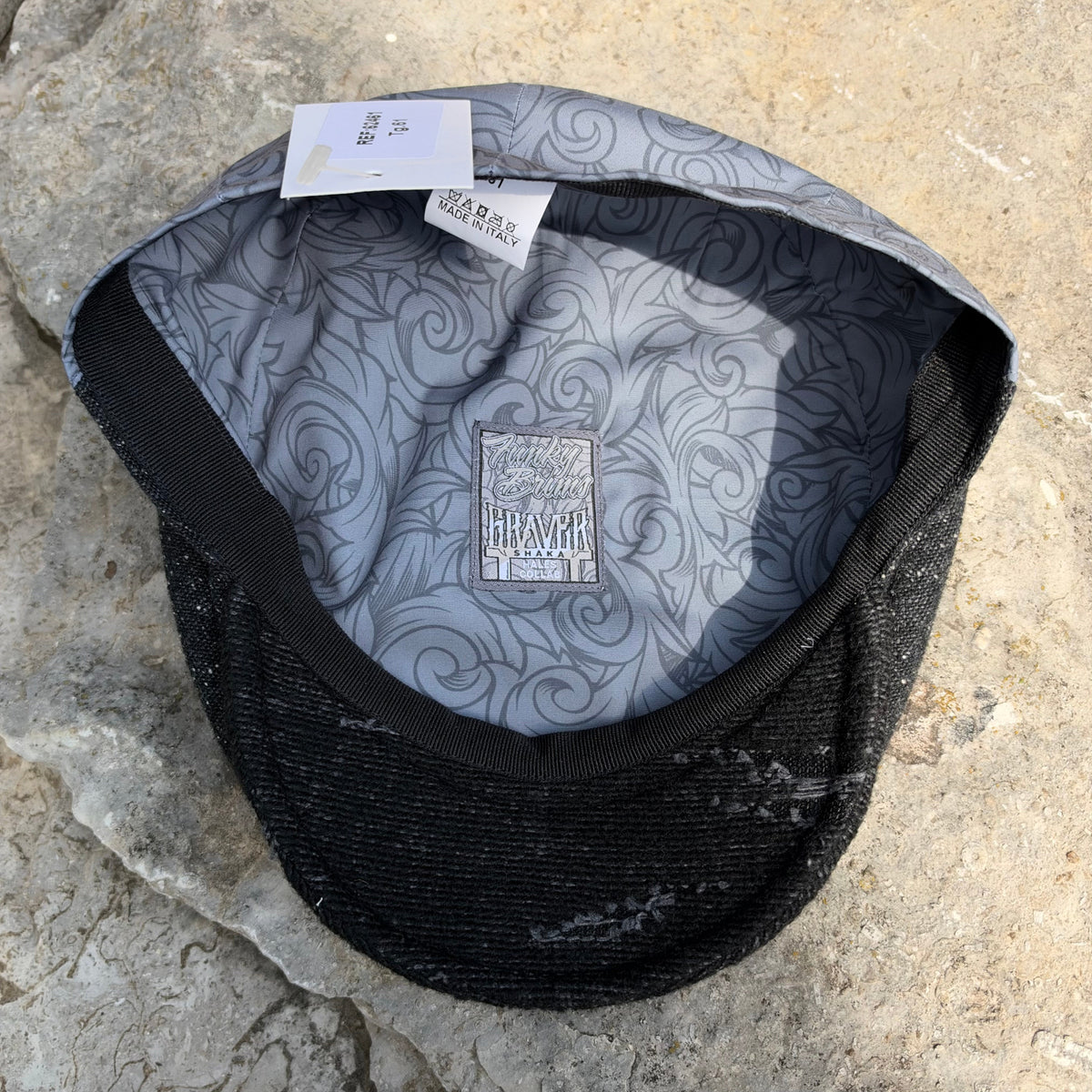A black mesh-back cap with a gray patterned inner lining, laid flat on a textured stone surface. The brand name 'Graver' is visible on the inner label.