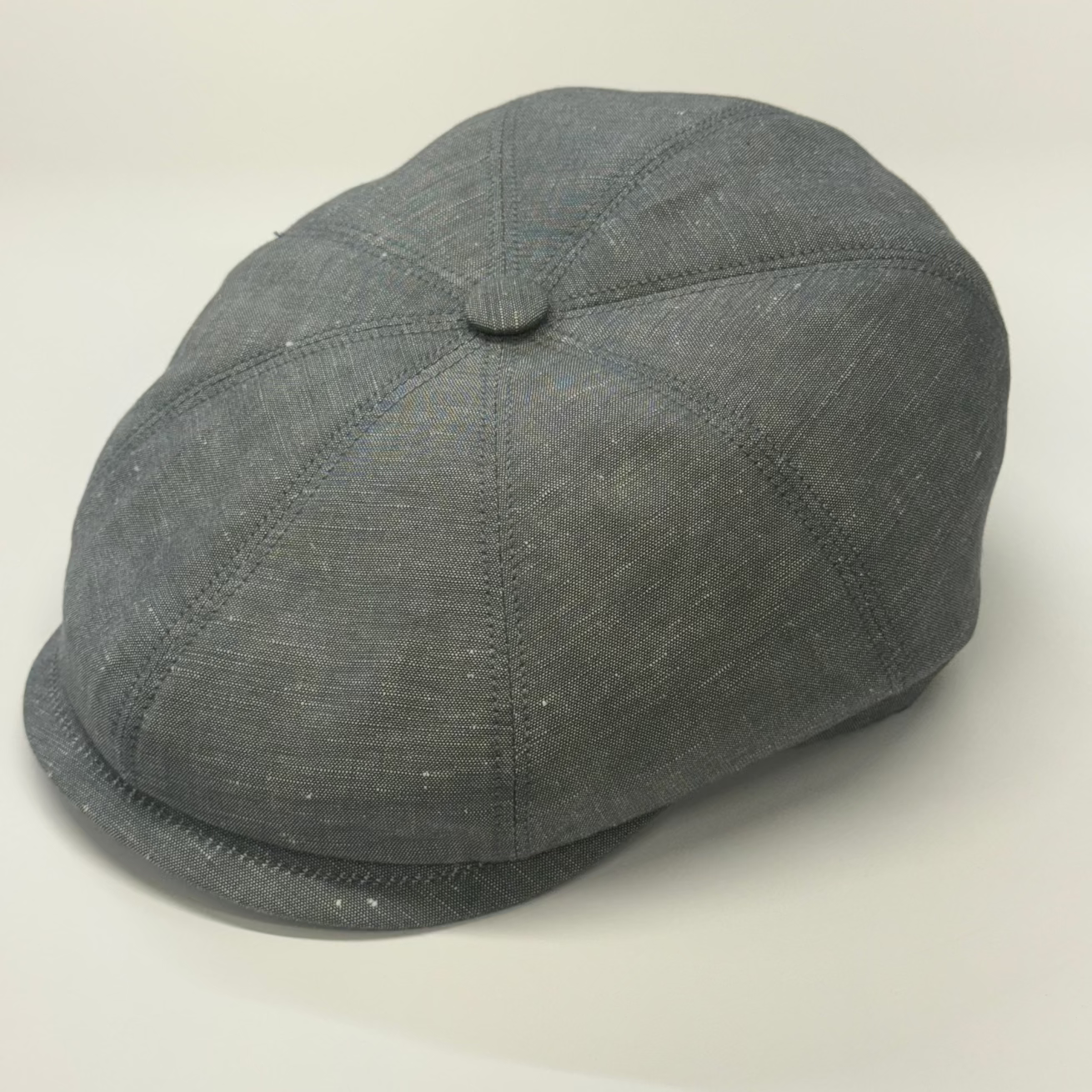 A dark gray textured flat cap with a button on top, photographed on a light neutral background.