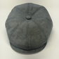 A dark gray textured flat cap with a button on top, photographed from a top-down angle on a light off-white background.