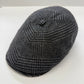 A dark gray and black houndstooth patterned flat cap, photographed on a plain white background.