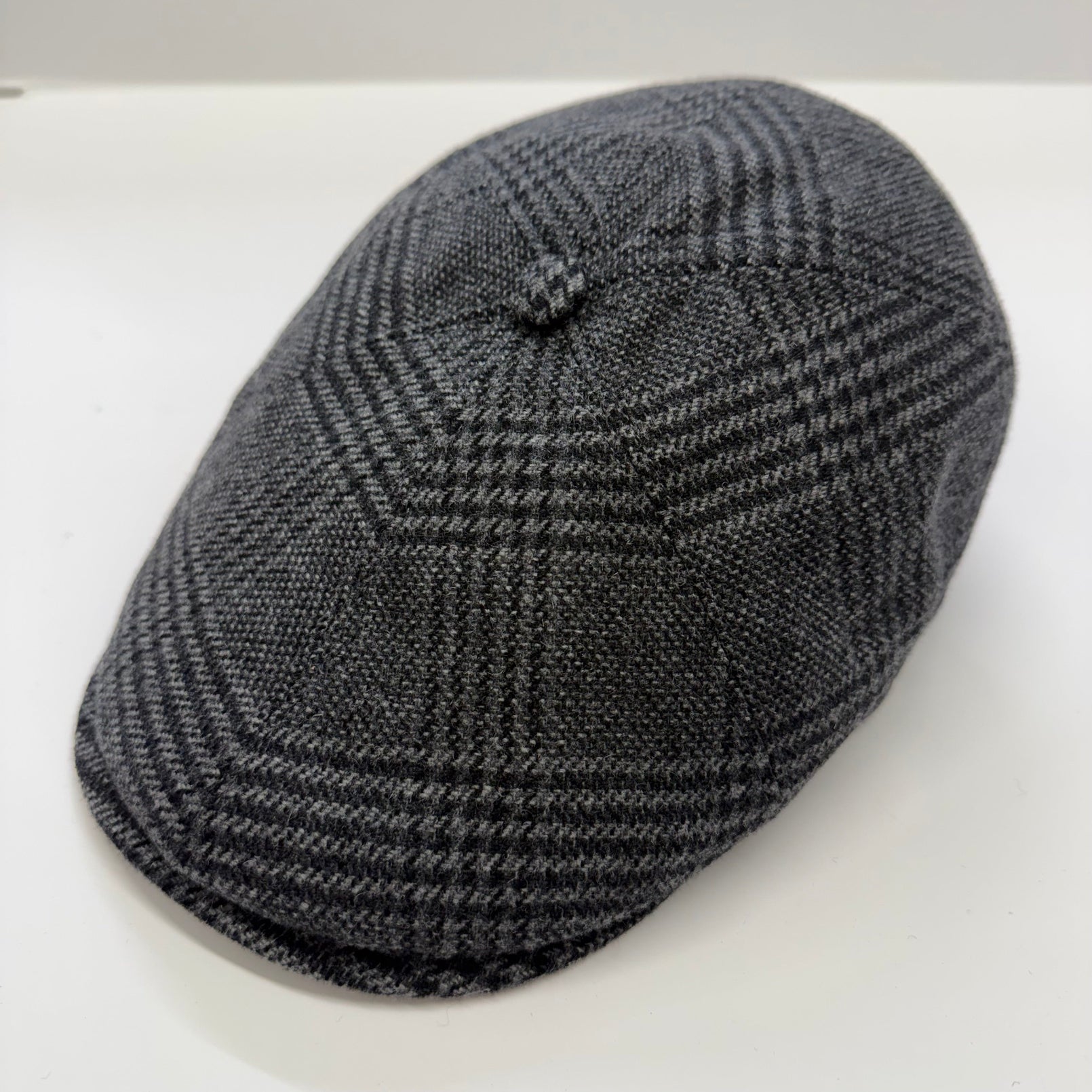 A dark gray and black houndstooth patterned flat cap, photographed on a plain white background.