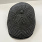 A dark gray and black houndstooth patterned flat cap with a button on top, photographed on a plain white surface.