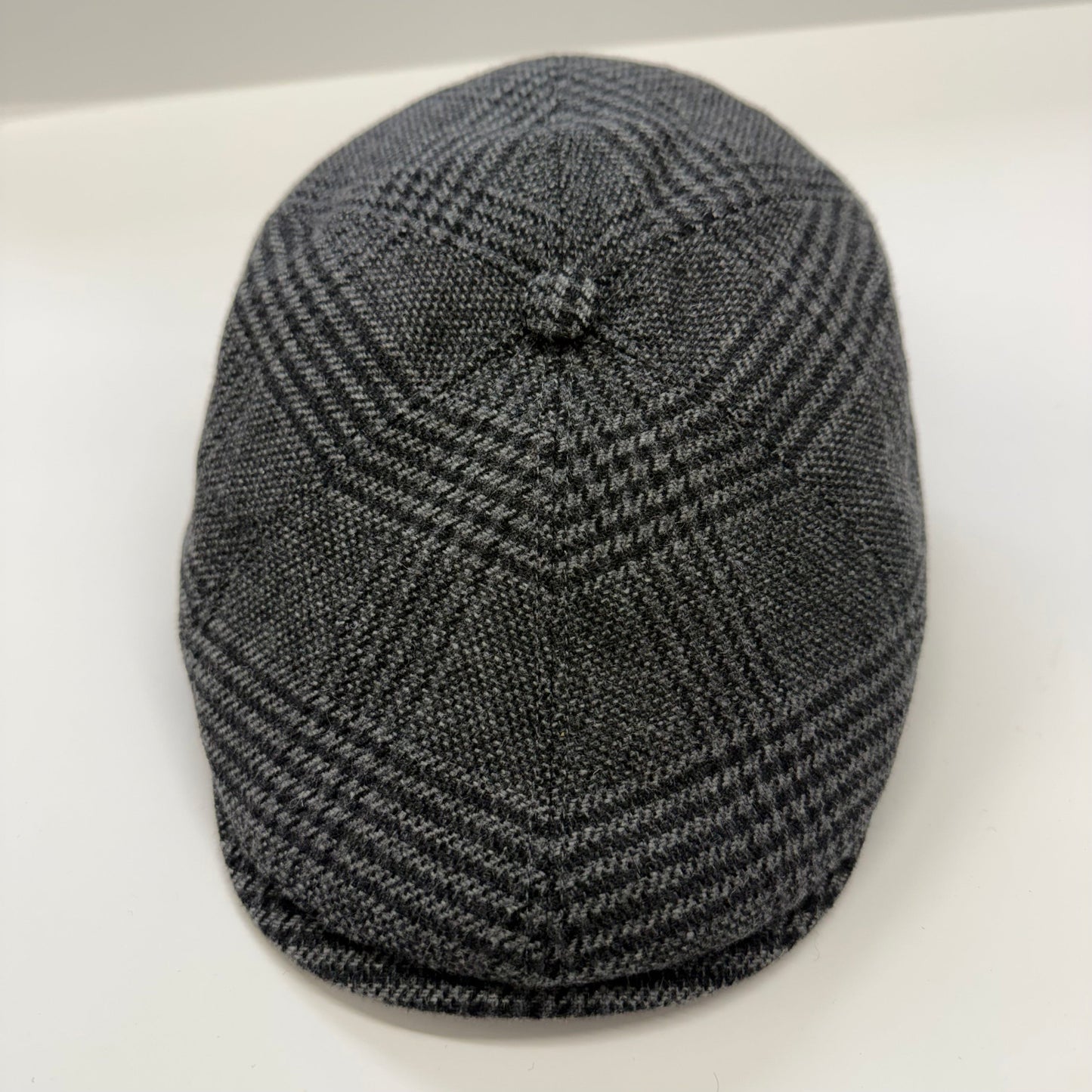 A dark gray and black houndstooth patterned flat cap with a button on top, photographed on a plain white surface.