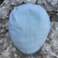 A light blue flat cap with a subtle white windowpane check pattern, photographed from above on a textured gray stone surface.