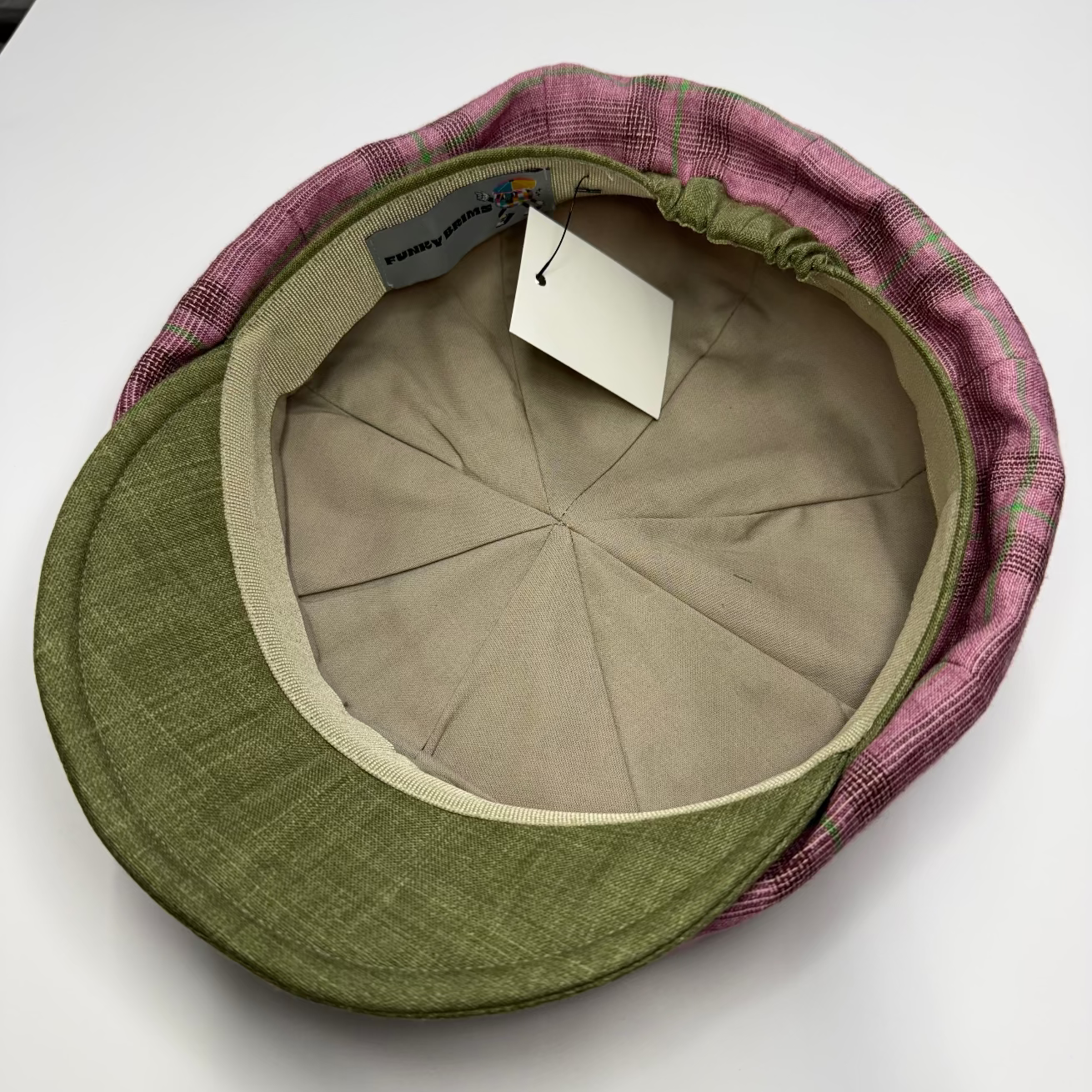 Green and pink checkered flat cap with brand label on a white background
