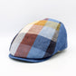 A structured flat cap with a multicolor plaid pattern featuring shades of blue, brown, yellow, and white, set against a plain white background.