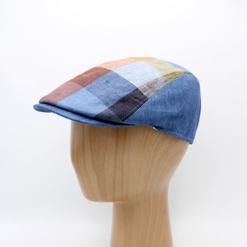 A denim flat cap with a multicolor plaid pattern on a wooden mannequin head against a white background.