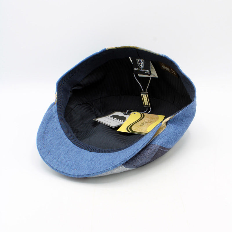 A blue denim flat cap shown from an overhead angle, revealing a dark navy interior and attached retail tags on a white background.