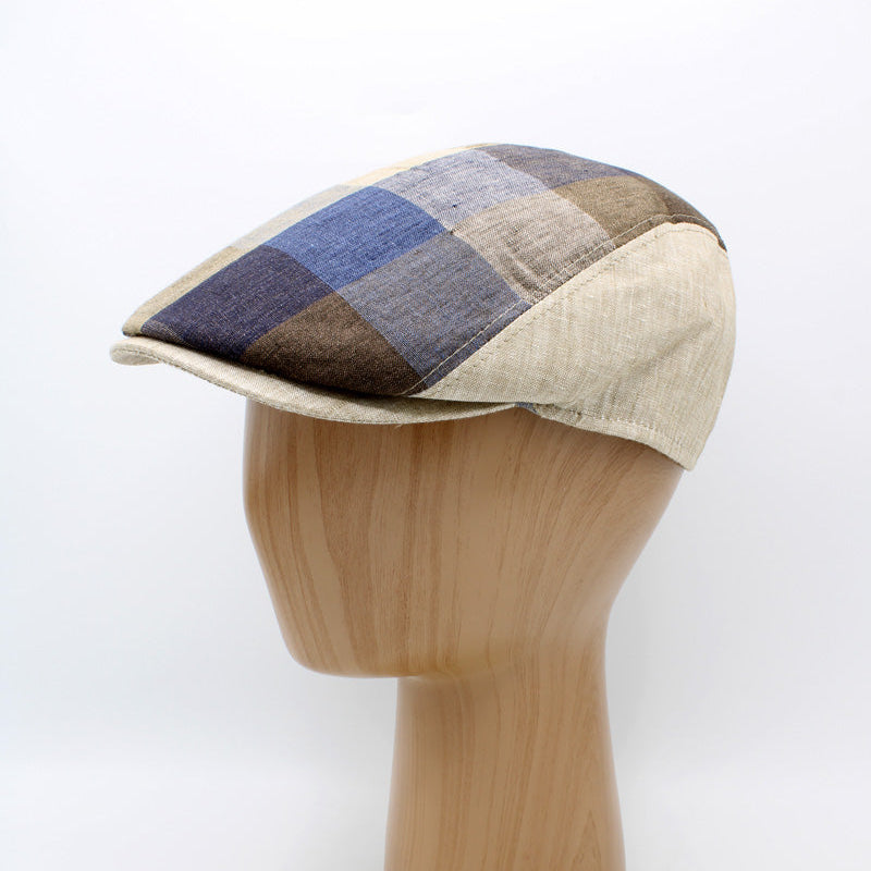 A patchwork check flat cap made of blue, brown, and beige woven fabrics, displayed on a light wood mannequin head against a white background.