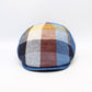 A structured flat cap with a multi-colored plaid pattern featuring shades of blue, beige, brown, and yellow, set against a plain white background.