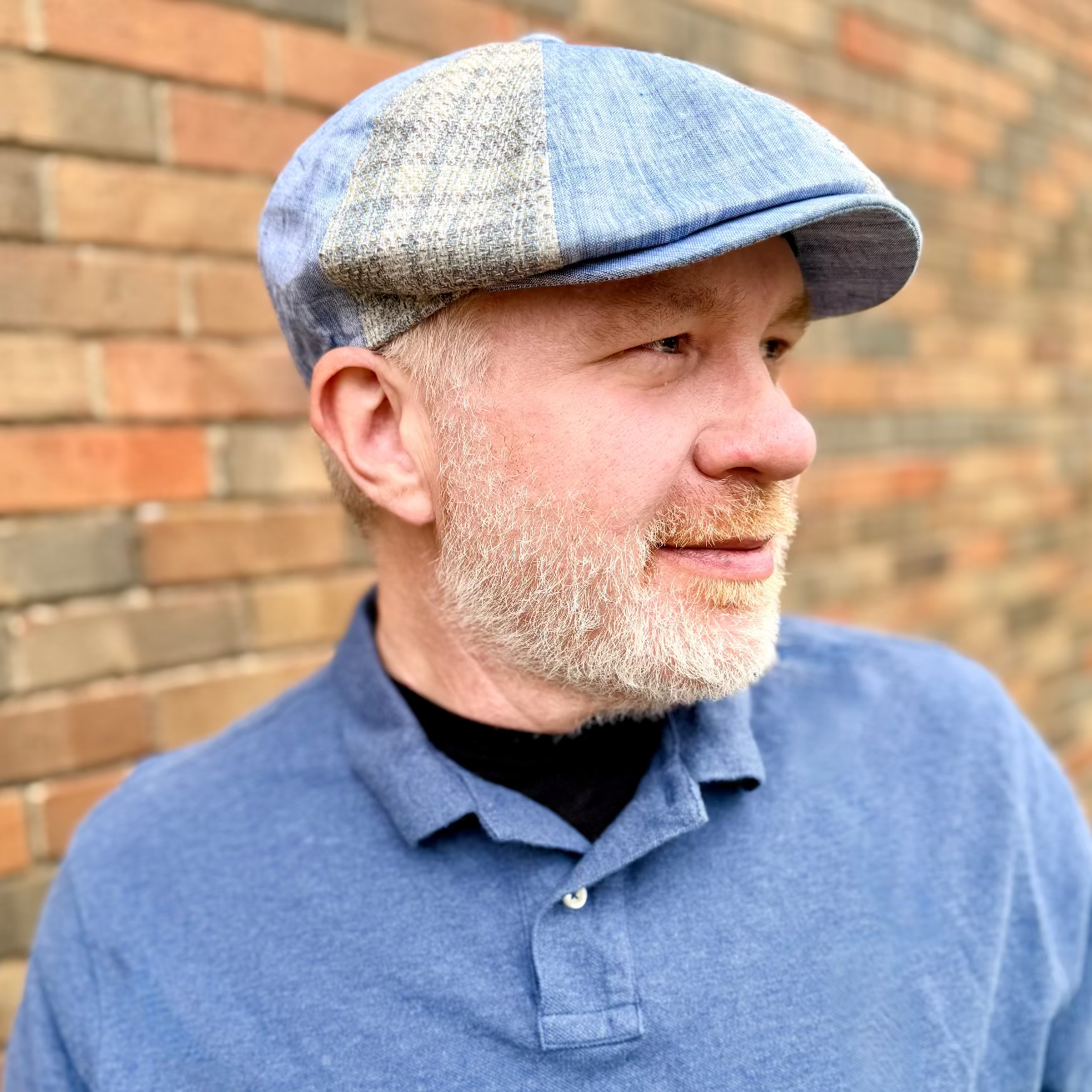 Man wearing a blue cap and matching polo shirt against a brick wall.