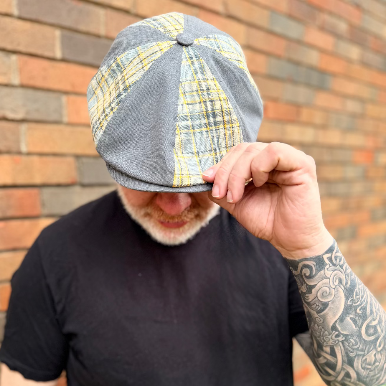 Person wearing a checkered cap in front of a brick wall