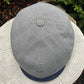 A top-down view of a classic flat cap with a black and white gingham pattern and a navy blue visor, resting on a textured white stone surface outdoors.