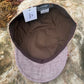 A flat-brim cap with a textured tweed exterior in muted pinkish-beige and brown, featuring a solid brown fabric interior and a white size tag, photographed outdoors on a large rock.