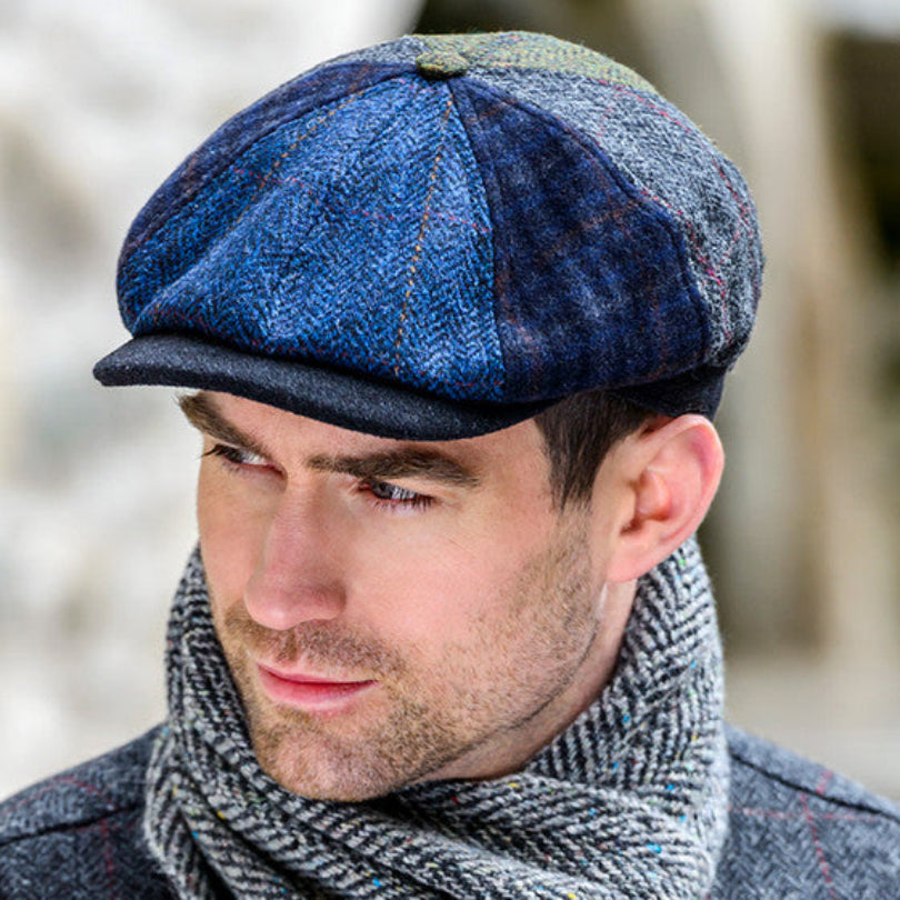 Man wearing a blue and green checkered cap and gray scarf outdoors.