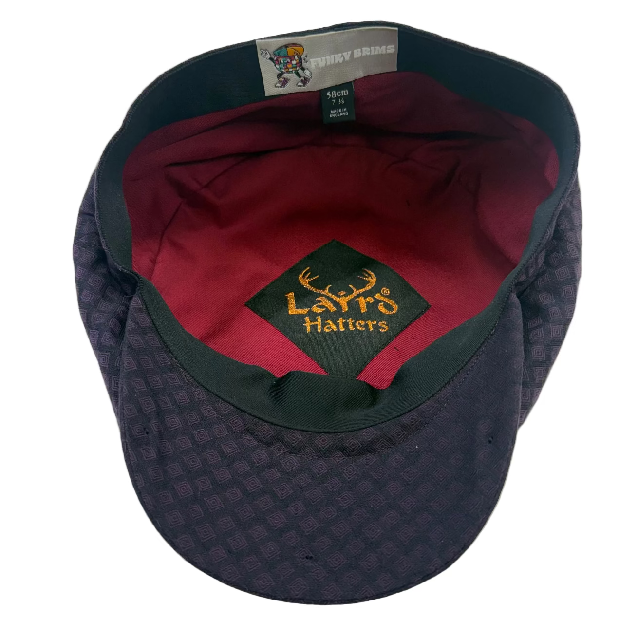 A dark purple and black patterned flat cap with a red interior lining. The inside features a black embroidered patch with yellow text reading 'Laird Hatters' and a gray brand tag at the top edge.