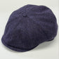 A dark purple and navy blue herringbone tweed flat cap, photographed on a clean white background.