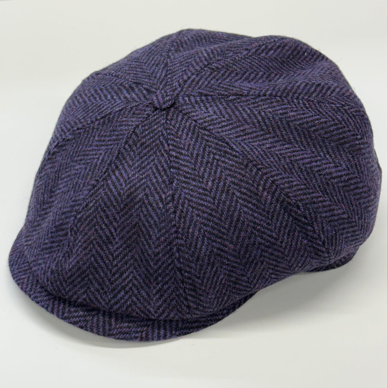 A dark purple and navy blue herringbone tweed flat cap, photographed on a clean white background.