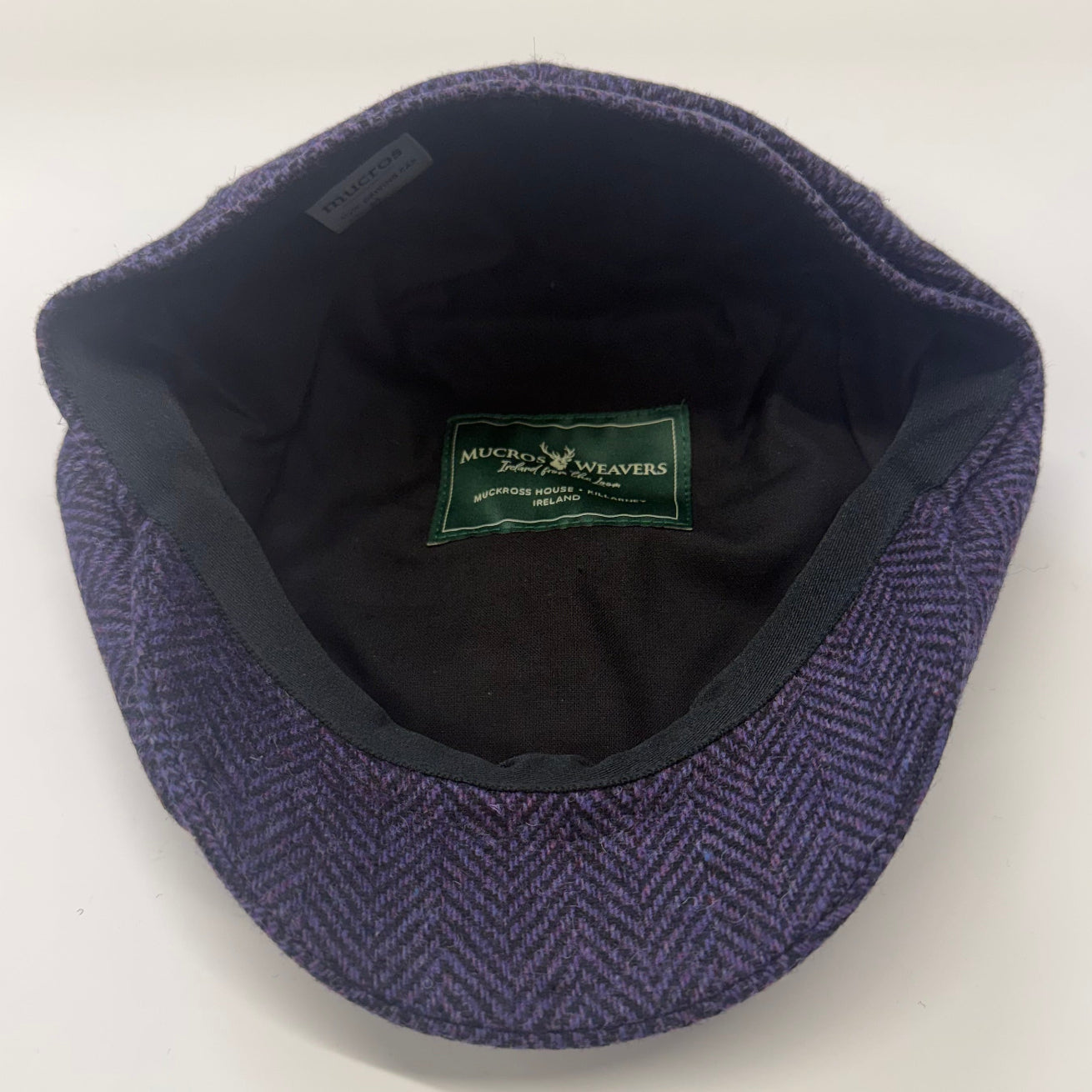 A vintage-style flat cap in a purple and blue herringbone pattern, shown from a top-down view on a white background. At FunkyBrims.