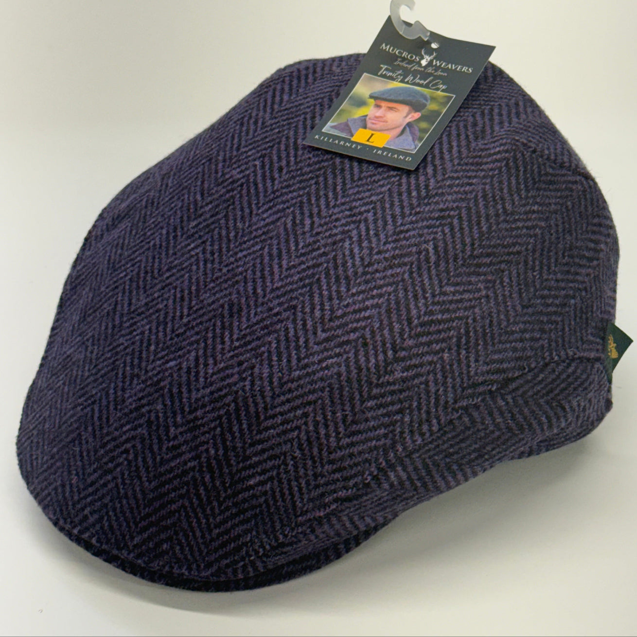 A dark navy blue herringbone tweed flat cap with a hangtag, photographed on a plain white background.