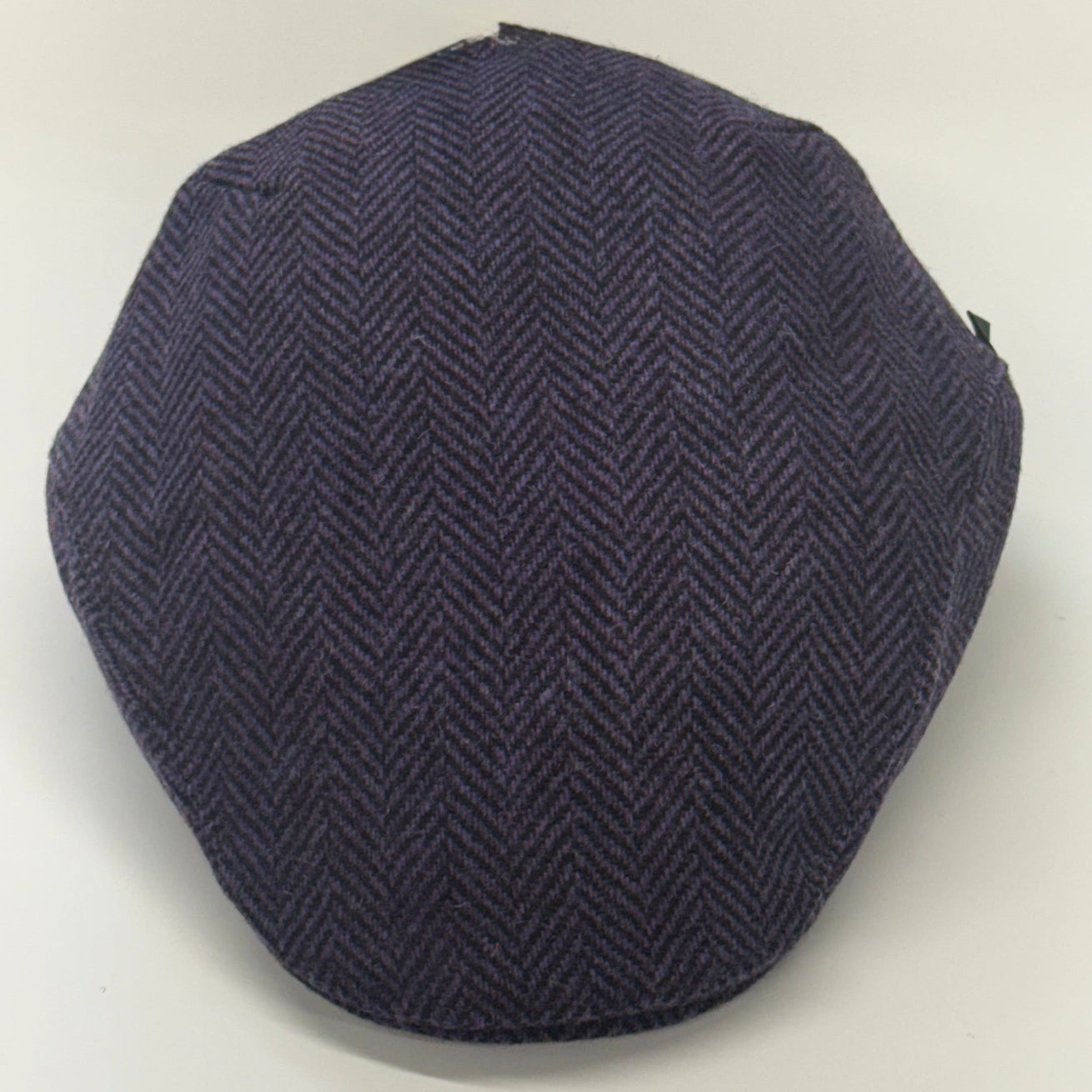 A dark purple herringbone pattern flat cap, photographed from a top-down angle on a plain white background.