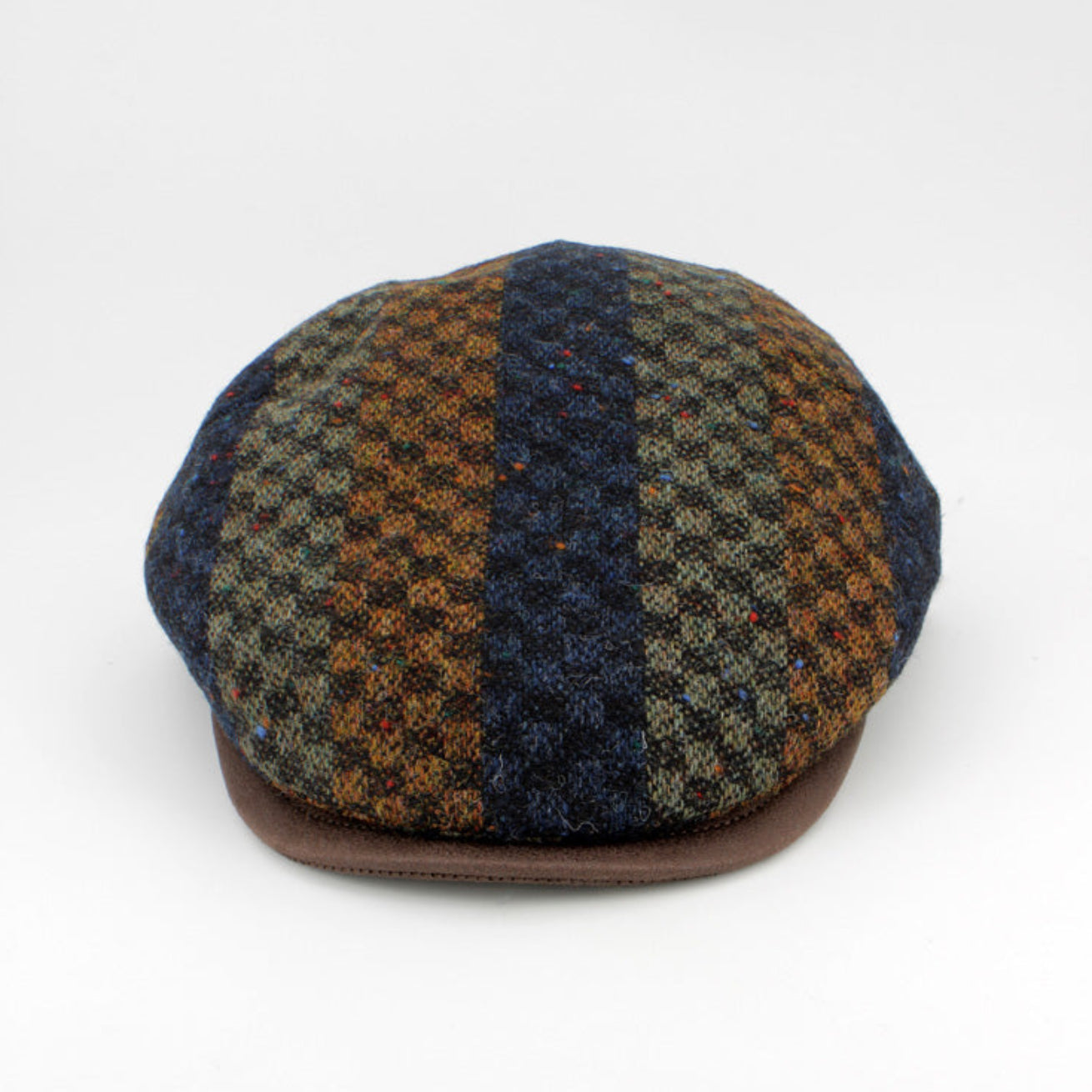 A flat cap made of a textured tweed fabric with vertical stripes of navy blue, brown, and olive green, featuring a solid brown visor, photographed on a light gray background.