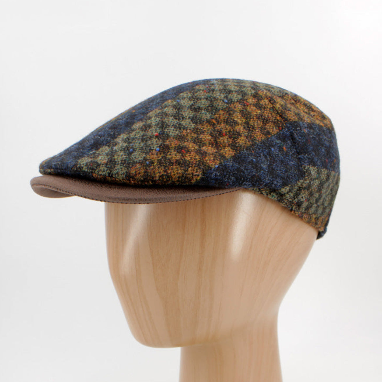 A vintage-style flat cap with a brown and blue houndstooth pattern, displayed on a light wood mannequin head against a white background.