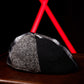 A black and gray patterned knit cap resting on a dark wooden surface, with a bright red geometric light fixture blurred in the background against a black setting.