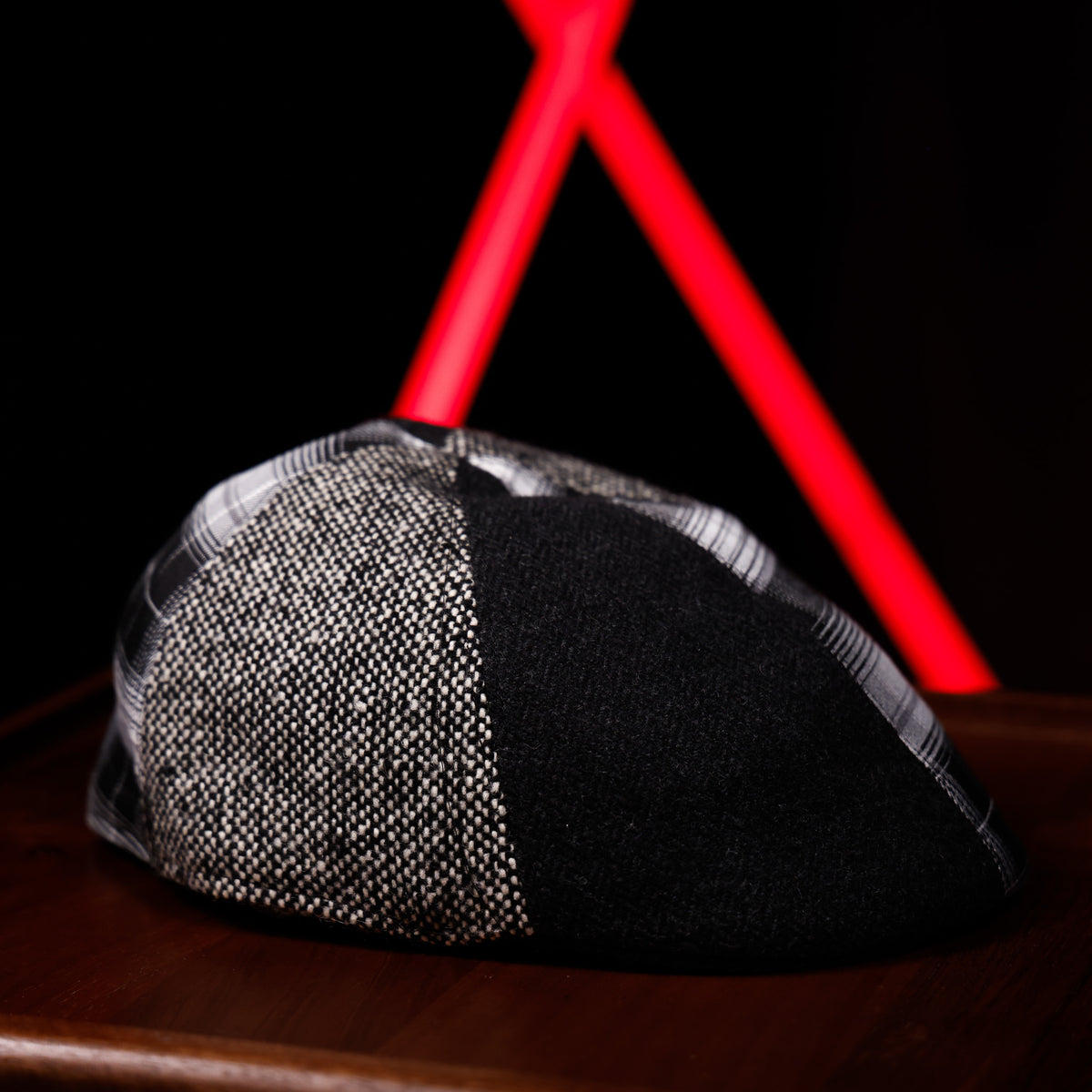 A black and gray patterned knit cap resting on a dark wooden surface, with a bright red geometric light fixture blurred in the background against a black setting.